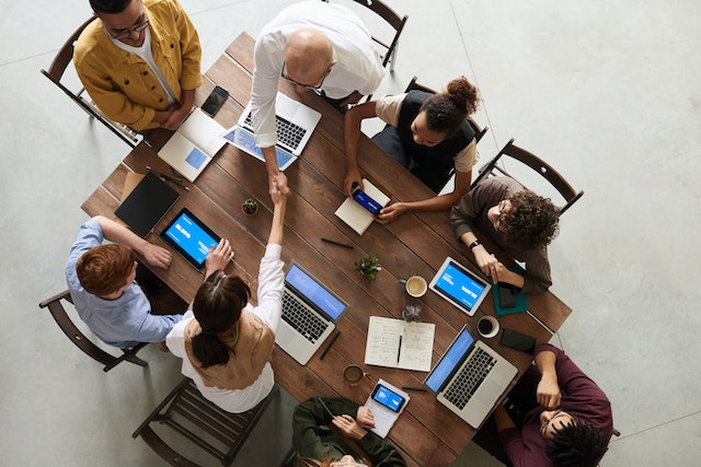 top down view of 8 business people meeting around a table with laptops, two are shaking hands