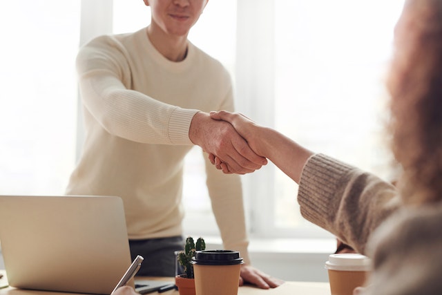 two business people shaking hands over desk with laptop in foreground